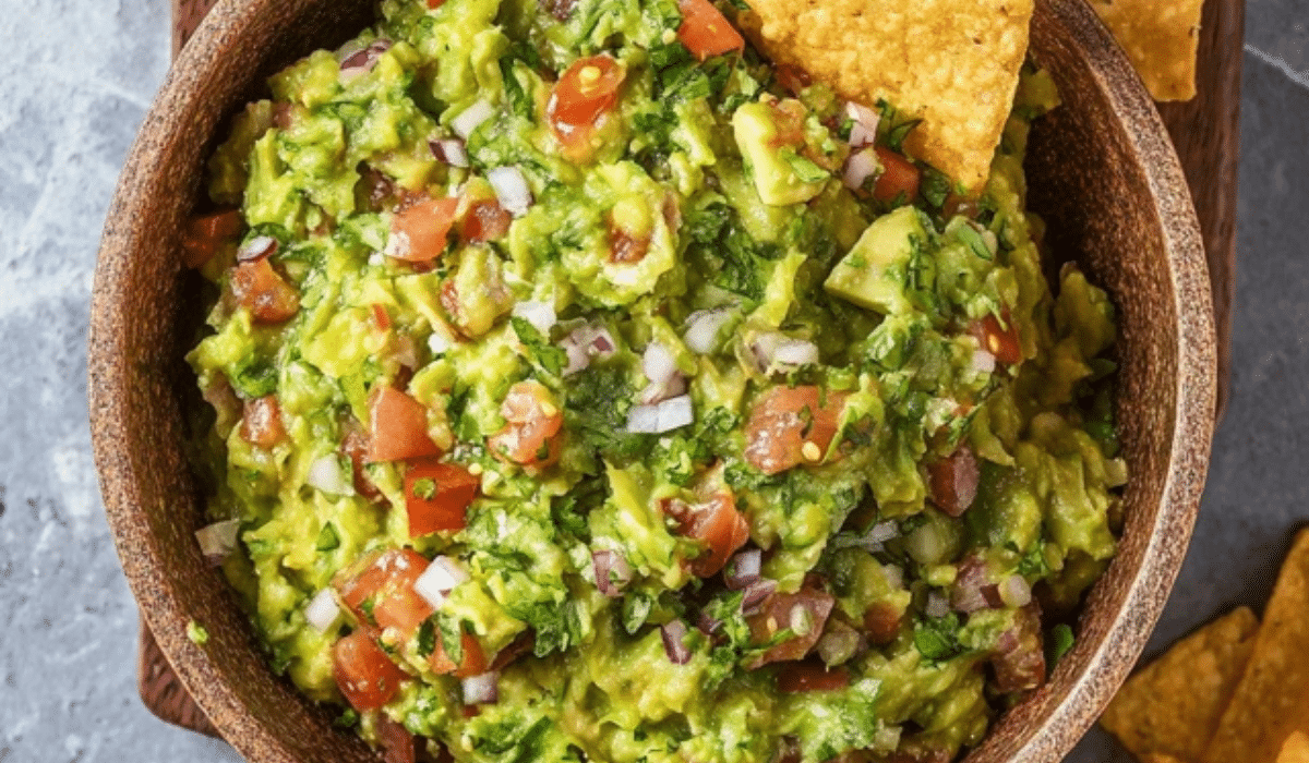 Chunky guacamole recipe in a bowl with chips, tomato, onion, and cilantro